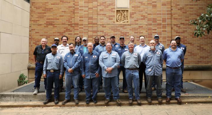 Electrical Distribution and Elevator Services staff pose together in front of a brick wall on the UT Austin campus.